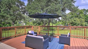 A deck with wicker furniture, a blue umbrella, and a wooden railing. - Downtown Boerne Home on Cibolo Creek w/ Fire Pit (Boerne)