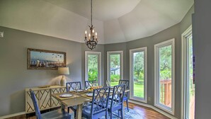A dining area with a table set for four, surrounded by chairs with a crisscross back design, a chandelier, and a painting on the wall. - Downtown Boerne Home on Cibolo Creek w/ Fire Pit (Boerne)