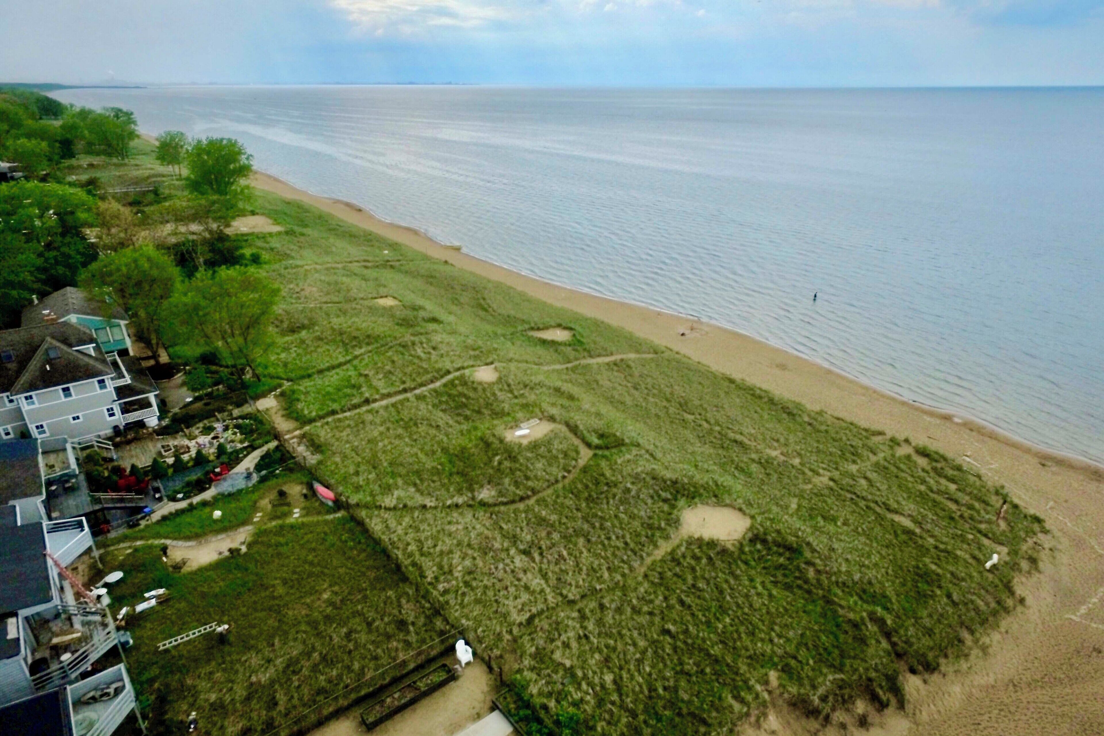 A coastal area with a sandy beach, grassy terrain, and a few buildings.