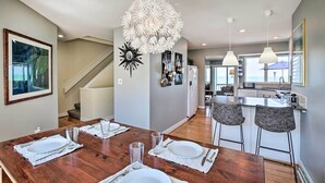 A modern kitchen with a central island, a dining area with a wooden table set for four, and a staircase leading to another level. - Lakefront Family Retreat w/ Grill: Steps to Beach! (Gary)