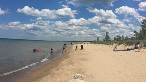 A beach with people swimming and walking along the shore. - Lakefront Family Retreat w/ Grill: Steps to Beach! (Gary)