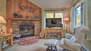 Una sala de estar con chimenea de ladrillo, televisor, un sillón cómodo y una mesa de centro de madera.