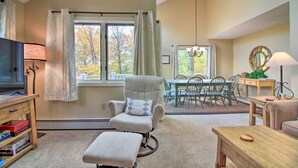 Una sala de estar acogedora con televisor, sillón mecedora, mesa de comedor con sillas y ventana con cortinas.