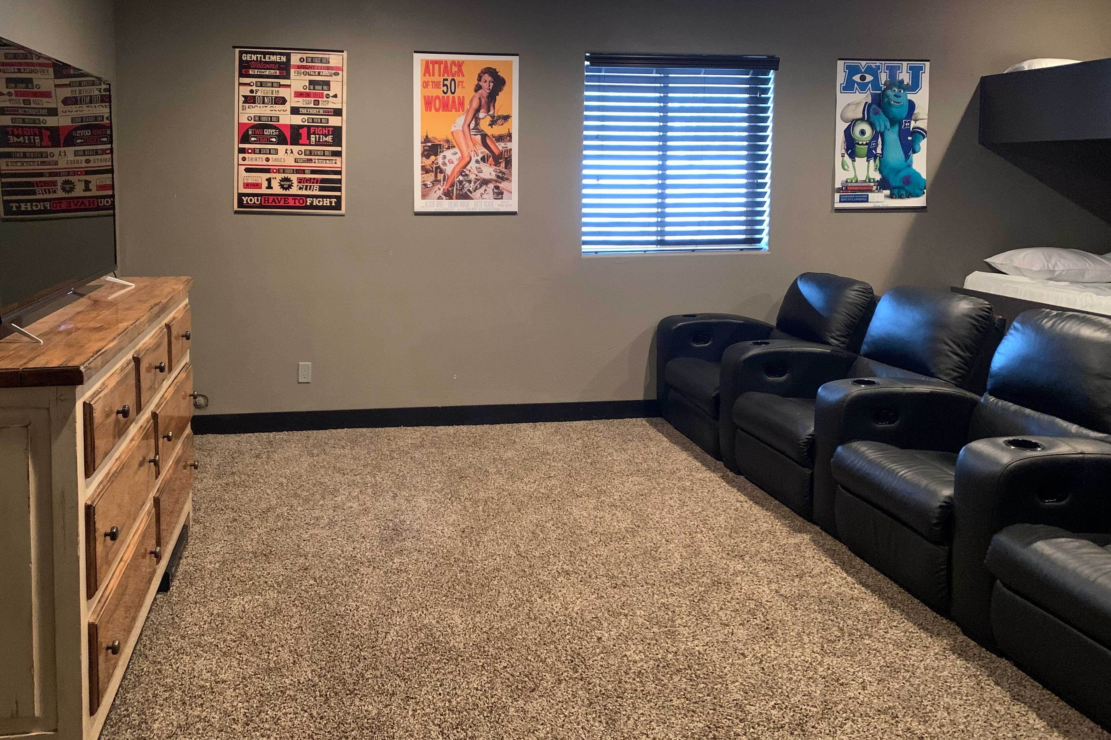 Een kamer met een vloerbedekking, een houten dressoir, zwarte leren fauteuils en drie posters aan de muur.