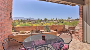 A patio with a round metal table and chairs, a brick wall, and a view of a desert landscape with mountains in the distance. - Sun-soaked AZ Townhome w/ Private Patio & Mtn View (Green Valley)