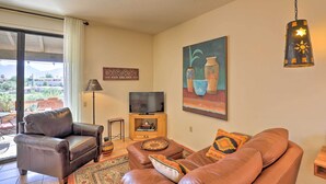 A living room with a leather sofa, a television on a wooden stand, and a painting on the wall. - Sun-soaked AZ Townhome w/ Private Patio & Mtn View (Green Valley)