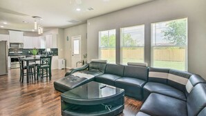 Un salon moderne avec un canapé d’angle, une table basse en verre et un coin repas avec des chaises.