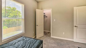 Une chambre avec un lit simple, une fenêtre avec des stores et un placard avec une tringle à vêtements.