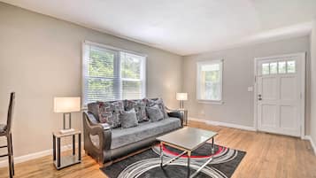 A modern living room with a grey sofa, two side tables with lamps, a coffee table, and a black rug with a red and white design.