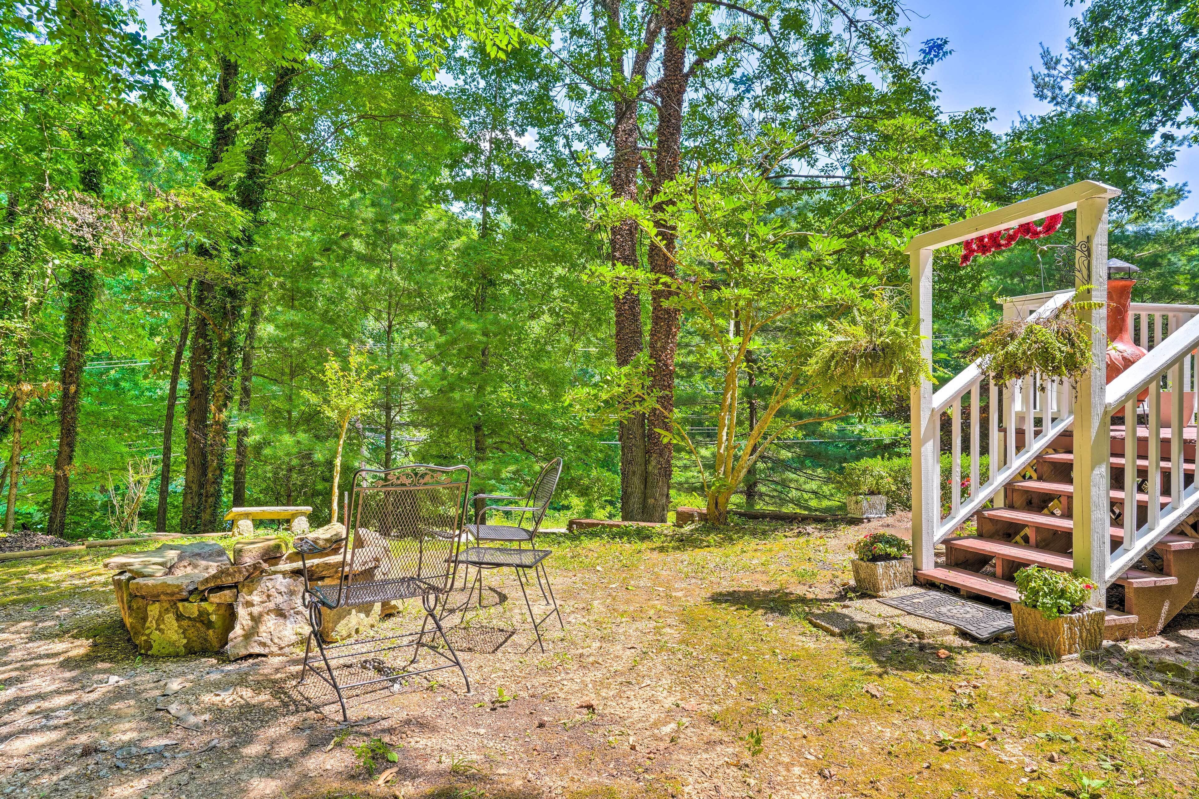 A forested area with a wooden staircase leading up to a red door, surrounded by trees and a picnic table with chairs.