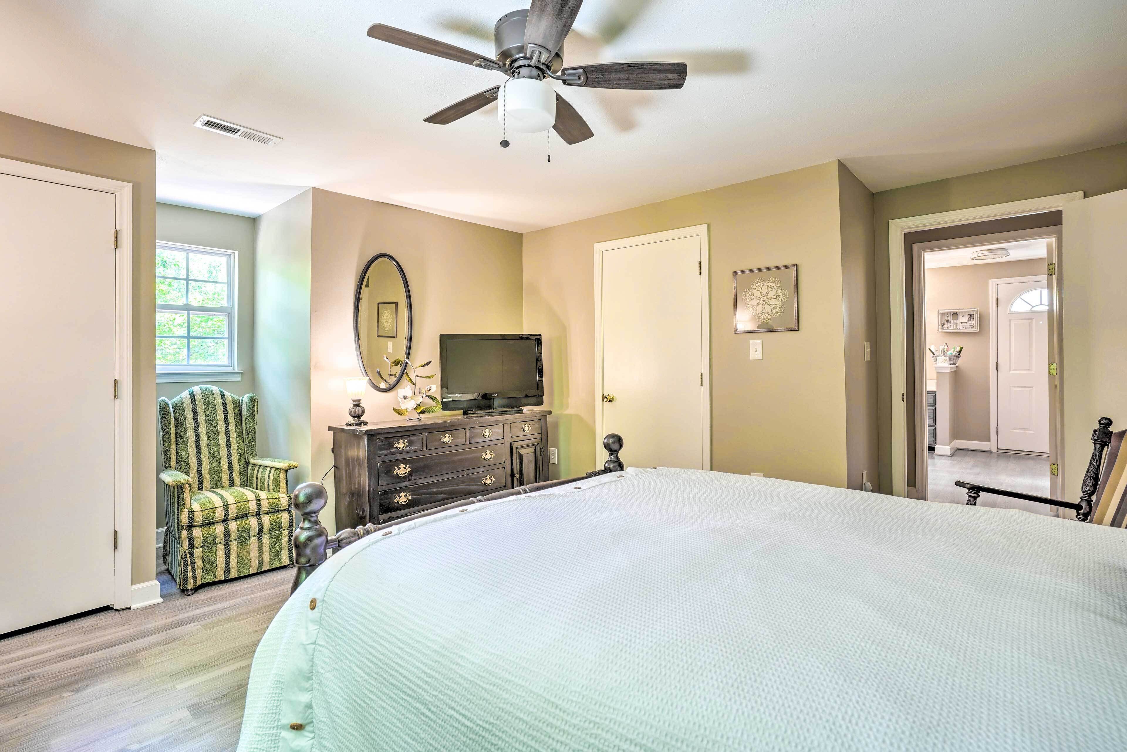 A bedroom with a large bed, a ceiling fan, a dresser, a television, and a chair.
