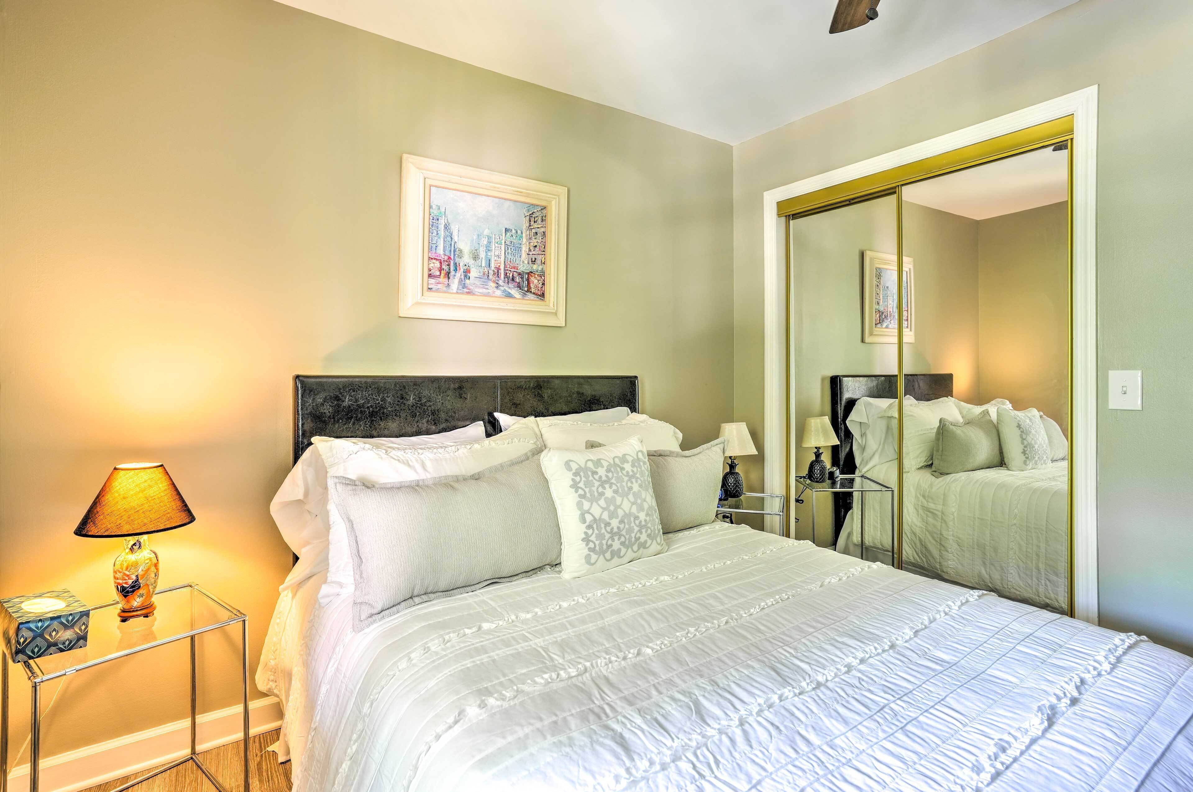 A bedroom with a bed, bedside tables, a mirror, and a painting on the wall.