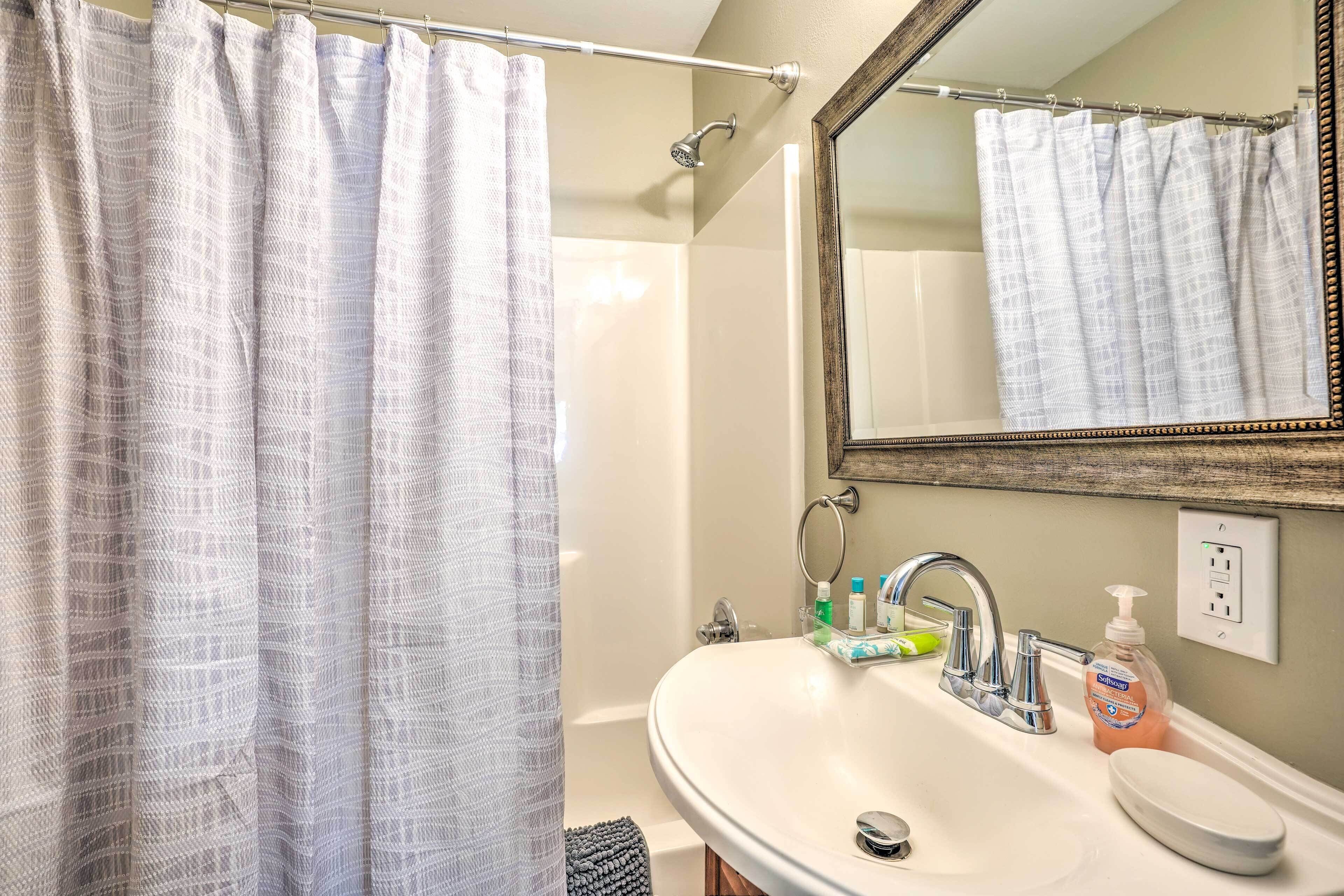 A bathroom with a shower curtain, a sink with a mirror, and toiletries.