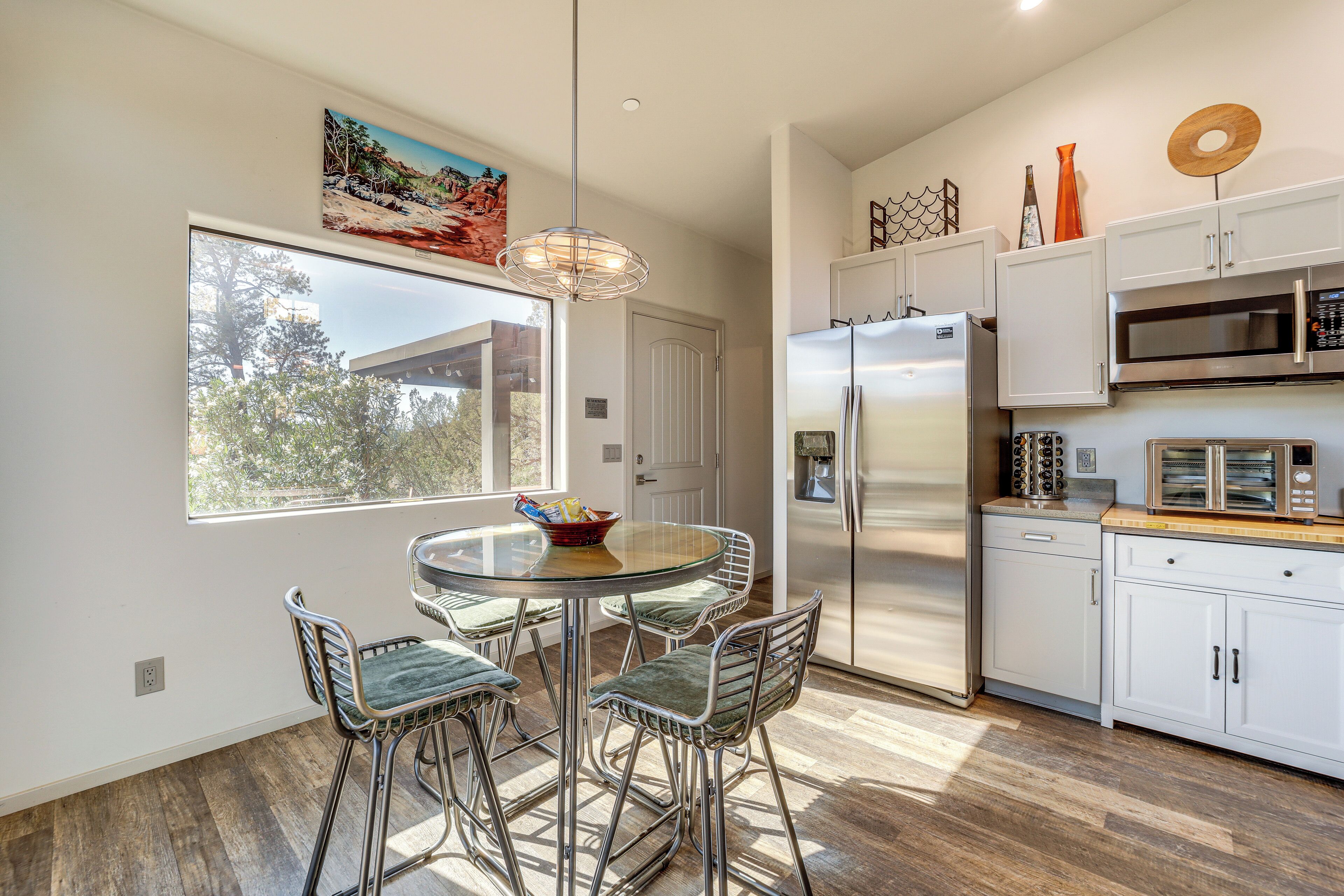Una cocina moderna con armarios blancos, electrodomésticos de acero inoxidable y una zona de comedor con sillas de metal y una mesa de vidrio.