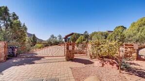 A gated entrance with a metal gate, a stone wall, and a paved driveway leading to a house. - Chic Sedona Retreat: 2 Mi to Cathedral Rock Trail! (Sedona)