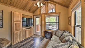 A spacious living area with a wooden ceiling, a large window, a fireplace, and a television. - Pagosa Springs Tiny Cabin: Fish, Hike, Ski & Soak! (Pagosa Springs)