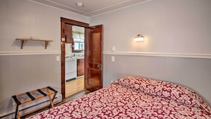 A bedroom with a bed, a wooden bench, a shelf, and a door leading to a kitchen. - Weirs Channel Cottage w/ Beach Access! (Laconia)