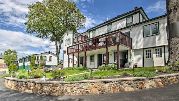 A two-story building with a balcony, stone retaining wall, and a tree in front. - Weirs Channel Cottage w/ Beach Access! (Laconia)