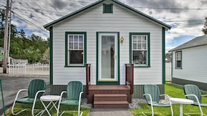 A small white building with green trim, a front door, and a small porch with green chairs and a table. - Weirs Channel Cottage w/ Beach Access! (Laconia)
