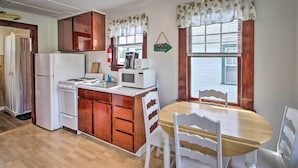 A compact kitchen with wooden cabinets, a white refrigerator, a microwave, and a dining table with white chairs. - Weirs Channel Cottage w/ Beach Access! (Laconia)