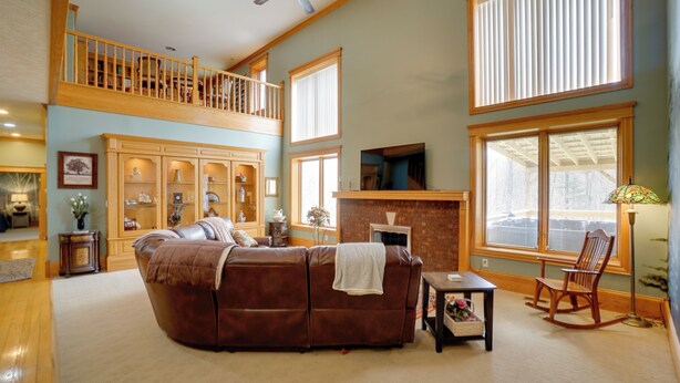 A spacious living room with a brown leather sofa, a fireplace, a wooden rocking chair, and a balcony with a wooden railing. - Hot Tub & Private Pond! Spacious Mcarthur Home (McArthur)