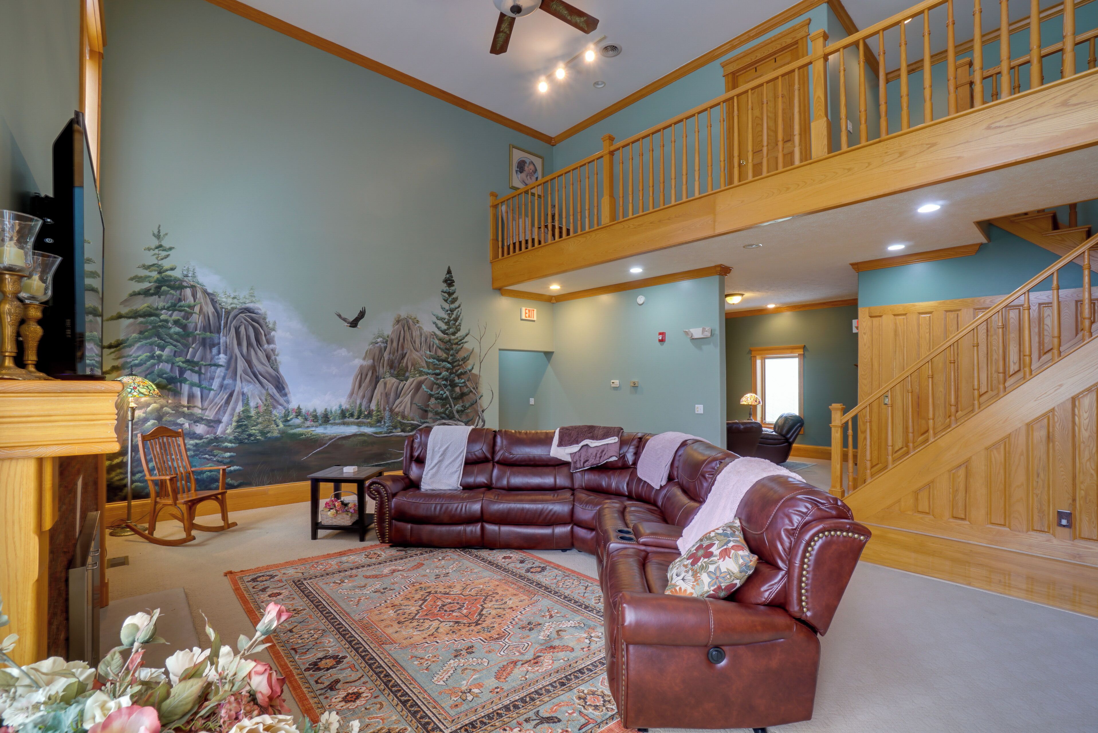 A spacious living room with a large sectional sofa, a wooden staircase, and a mural on the wall.