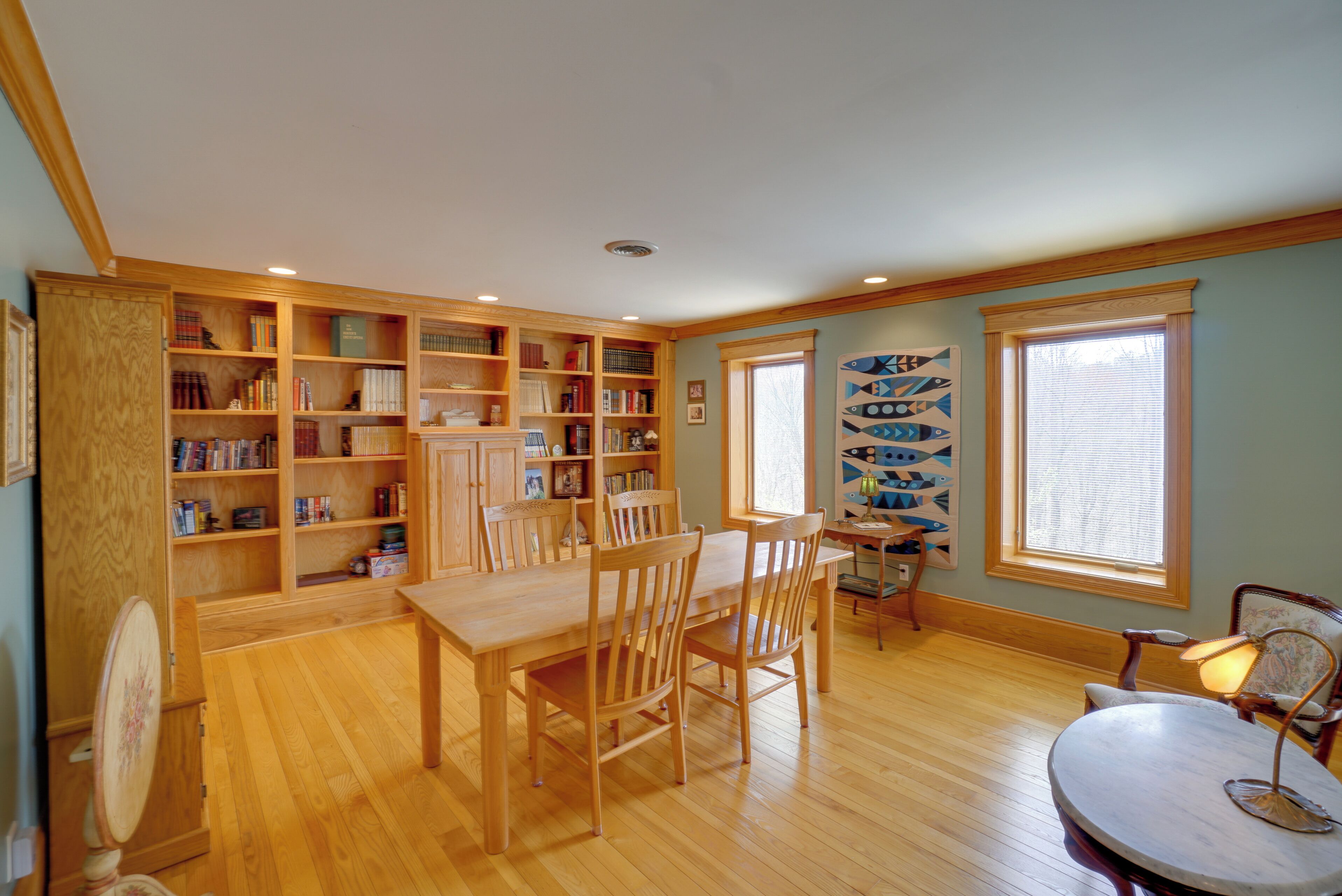 Una habitación amplia con una mesa de comedor de madera, sillas, una estantería y una ventana con persianas.