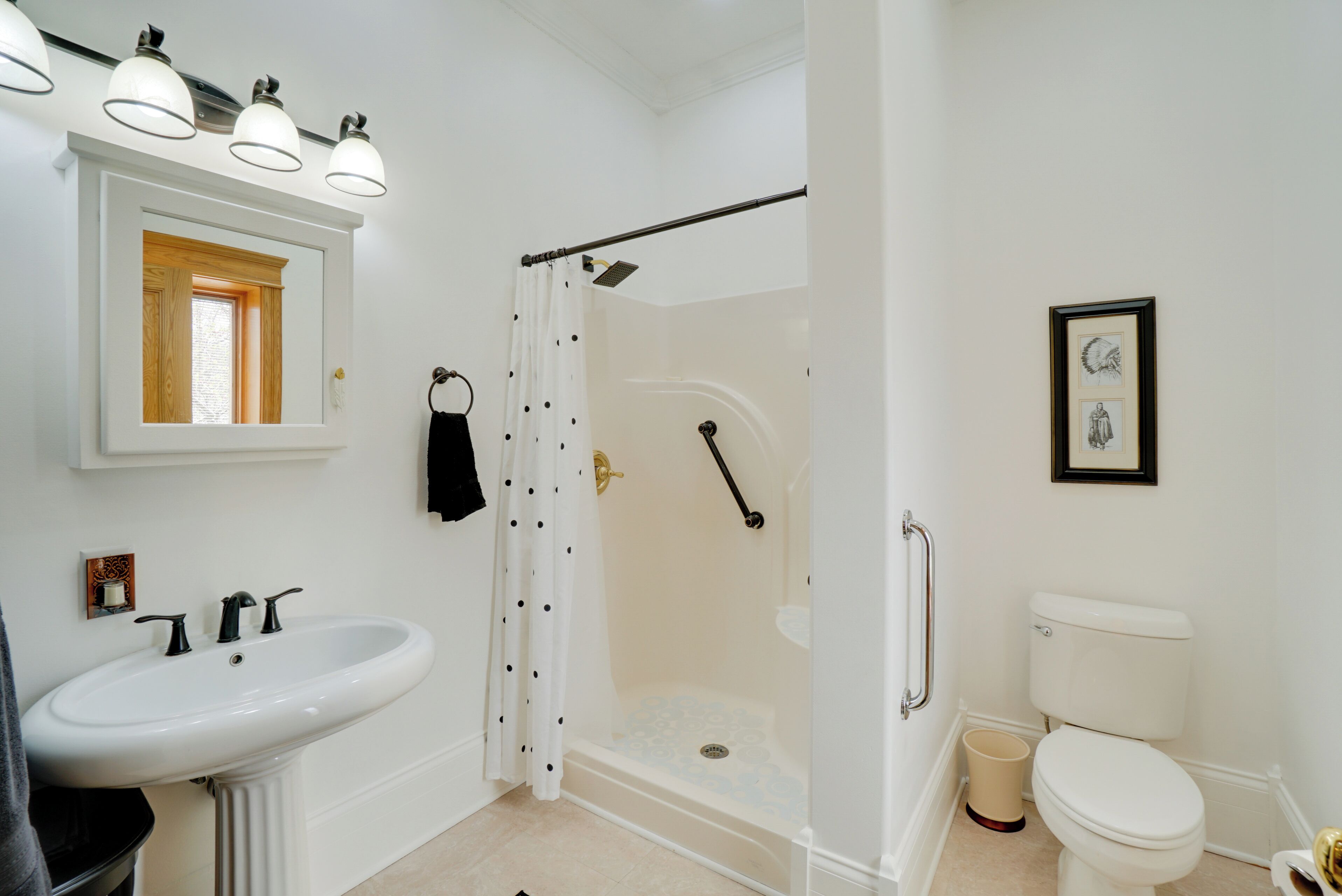 Une salle de bain avec un lavabo blanc, une douche avec une porte en verre, des toilettes et un tableau encadré au mur.