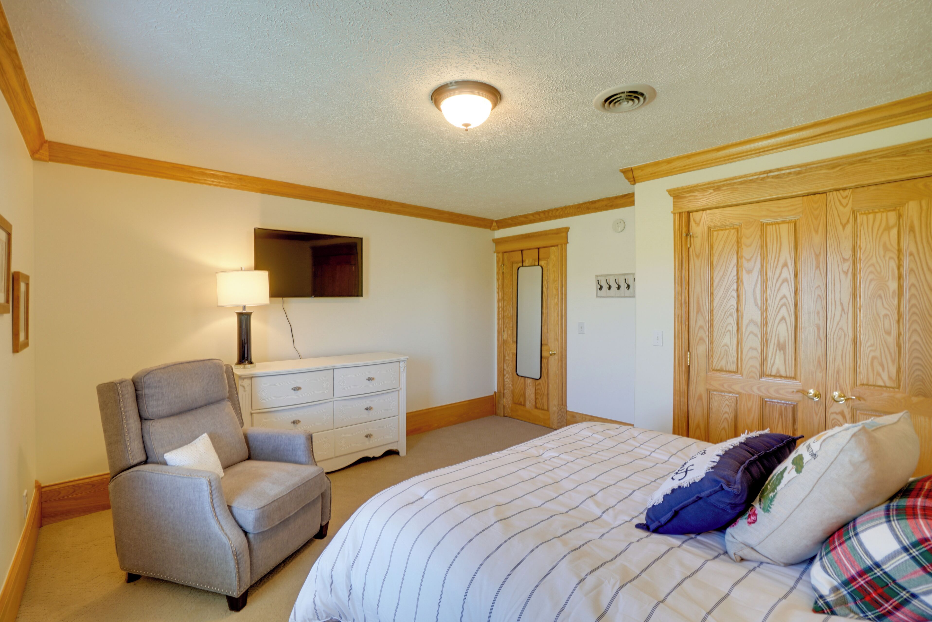 Un dormitorio con cama, una silla, cómoda, espejo y puerta.