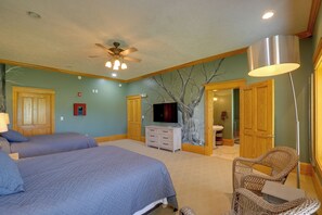 A bedroom with two beds, a ceiling fan, a TV, a dresser, and a wicker chair. - Hot Tub & Private Pond! Spacious Mcarthur Home (McArthur)