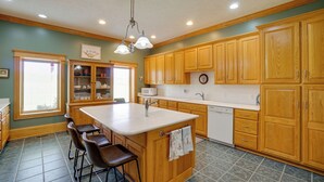 A kitchen with wooden cabinets, a central island with stools, a sink, and a microwave. - Hot Tub & Private Pond! Spacious Mcarthur Home (McArthur)