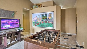 Ein Wohnzimmer mit einer Fußballstoßmaschine, einem Flachbildfernseher und einem großen gerahmten Poster des 'Yuma Agricultural Center Arizona'.