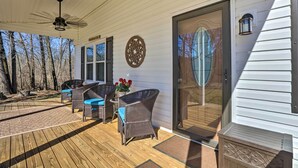 A covered deck with wicker furniture and a ceiling fan, a decorative wall piece, and a sliding glass door. - Quaint Creekside Cottage w/ Porch & Backyard! (Lexington)