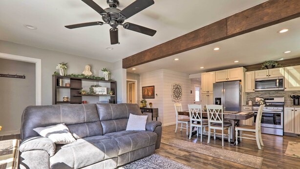 A modern living room with a gray sofa, a ceiling fan, and a dining area with a table and chairs. - Quaint Creekside Cottage w/ Porch & Backyard! (Lexington)