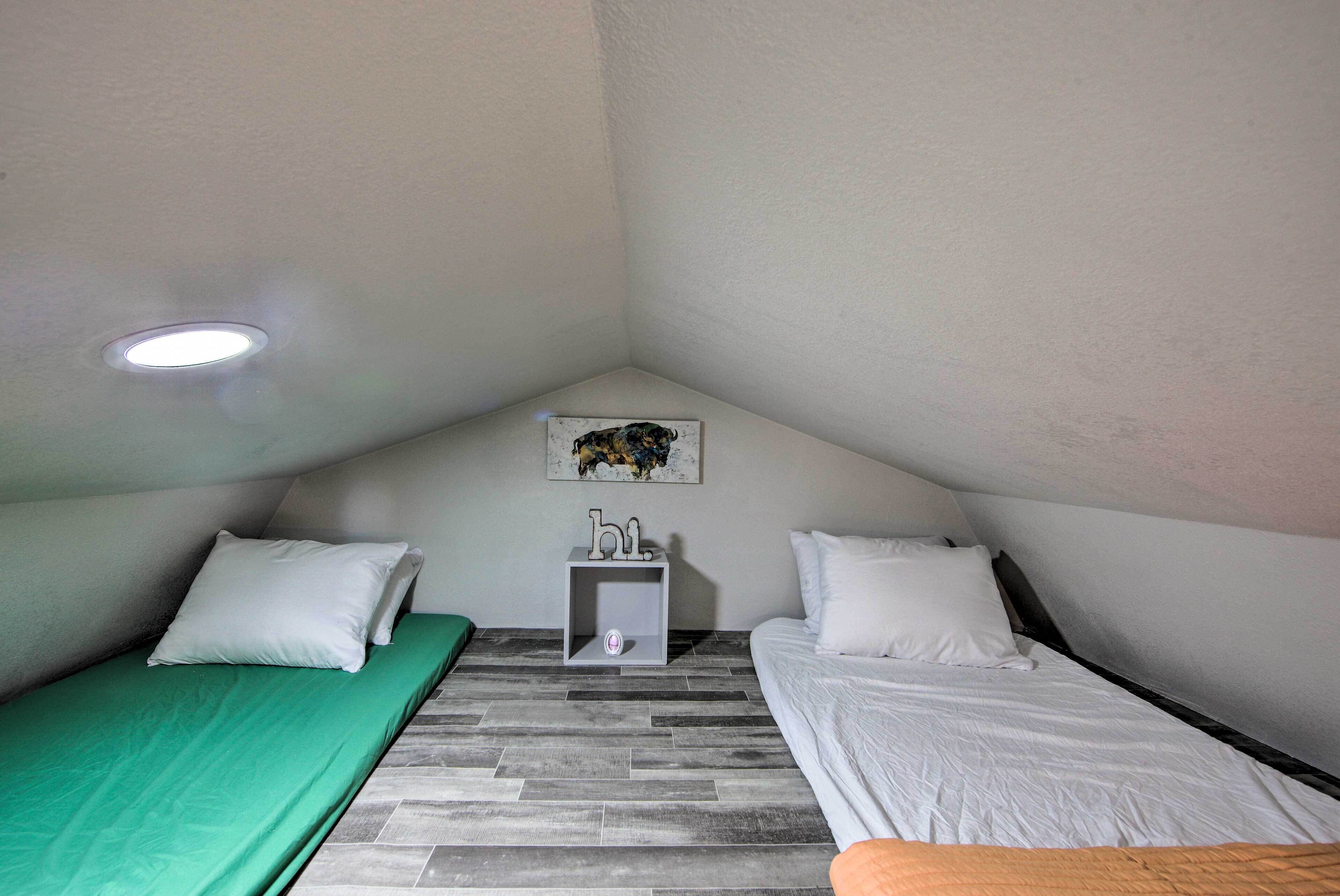 Una habitación pequeña y triangular con dos camas, una mesita de noche y una lámpara en el techo.