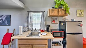 Una cocina compacta con encimera de madera, un lavamanos, un microondas, un refrigerador y una ventana con cortinas.
