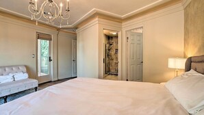 Un dormitorio espacioso con una cama grande, una araña de cristal, una zona de estar con un banco y un cuarto de baño con ducha.