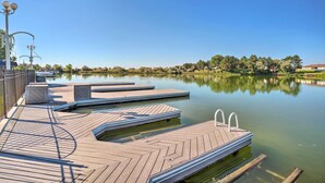 Un muelle de madera se adentra en un lago tranquilo, con reflejos nítidos, rodeado de árboles y un cielo despejado.