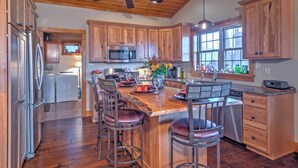 A modern kitchen with wooden cabinets, stainless steel appliances, and a central island with bar stools. - Beautiful Makanda Cabin in Shawnee National Forest (Makanda)