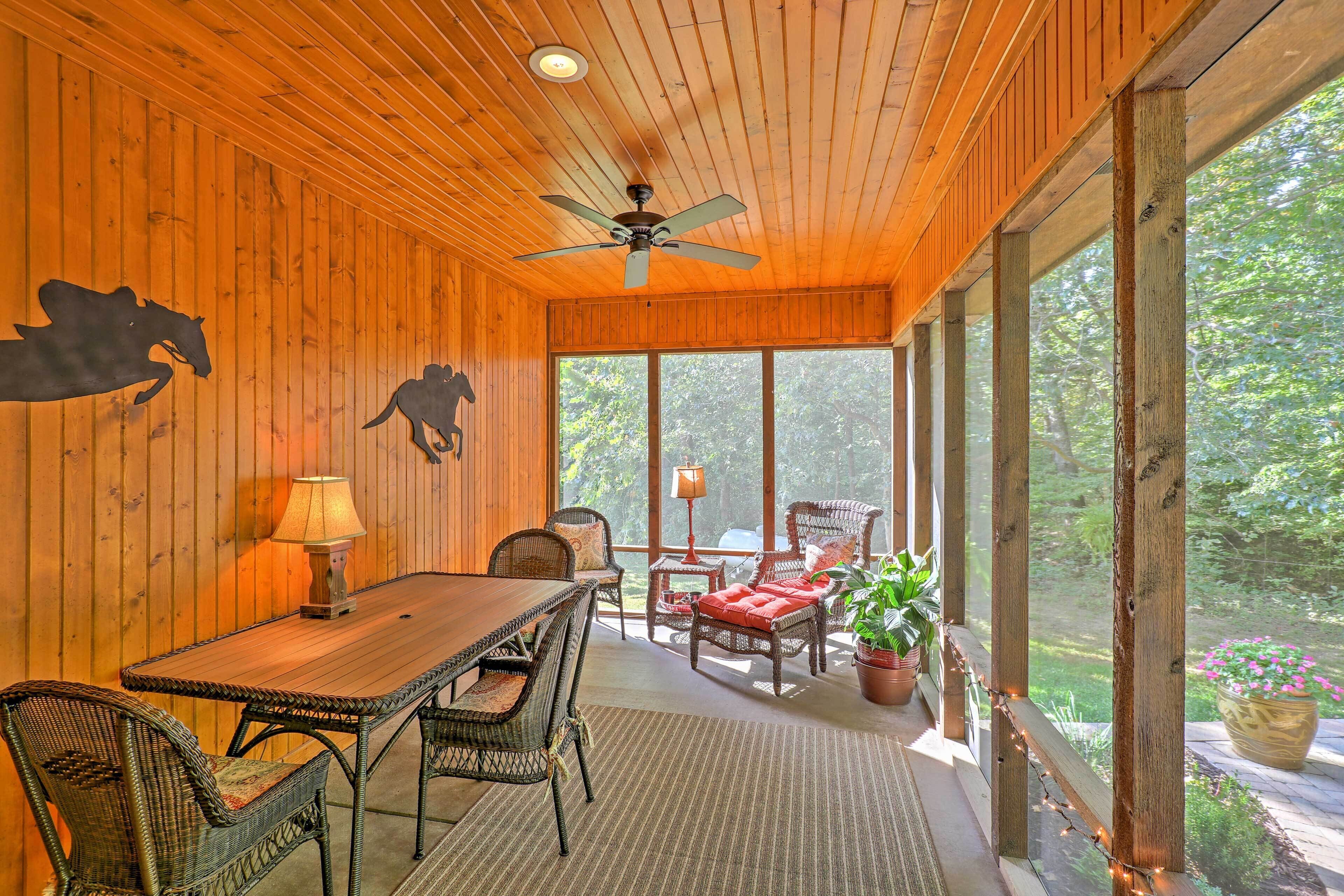 A wooden interior with a dining area, wicker furniture, and large windows.