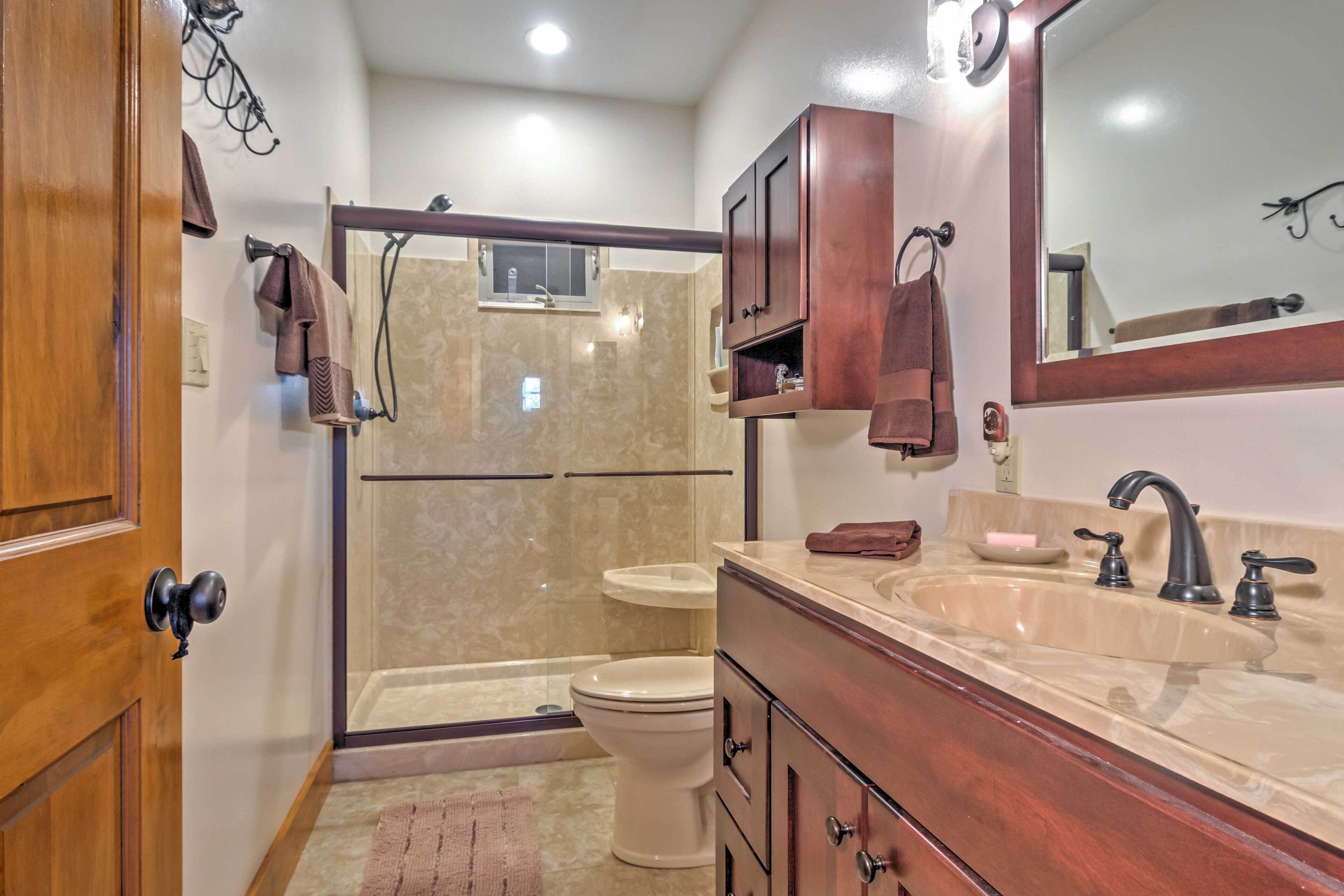 A bathroom with a shower, toilet, vanity, and a mirror.