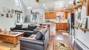 A spacious living room with a leather sofa, wooden coffee table, and a dining area. The kitchen features wooden cabinets and a stainless steel refrigerator. - 2 Mi to Fool Hollow Lake: Wooded Cabin w/ Fire Pit (Show Low)