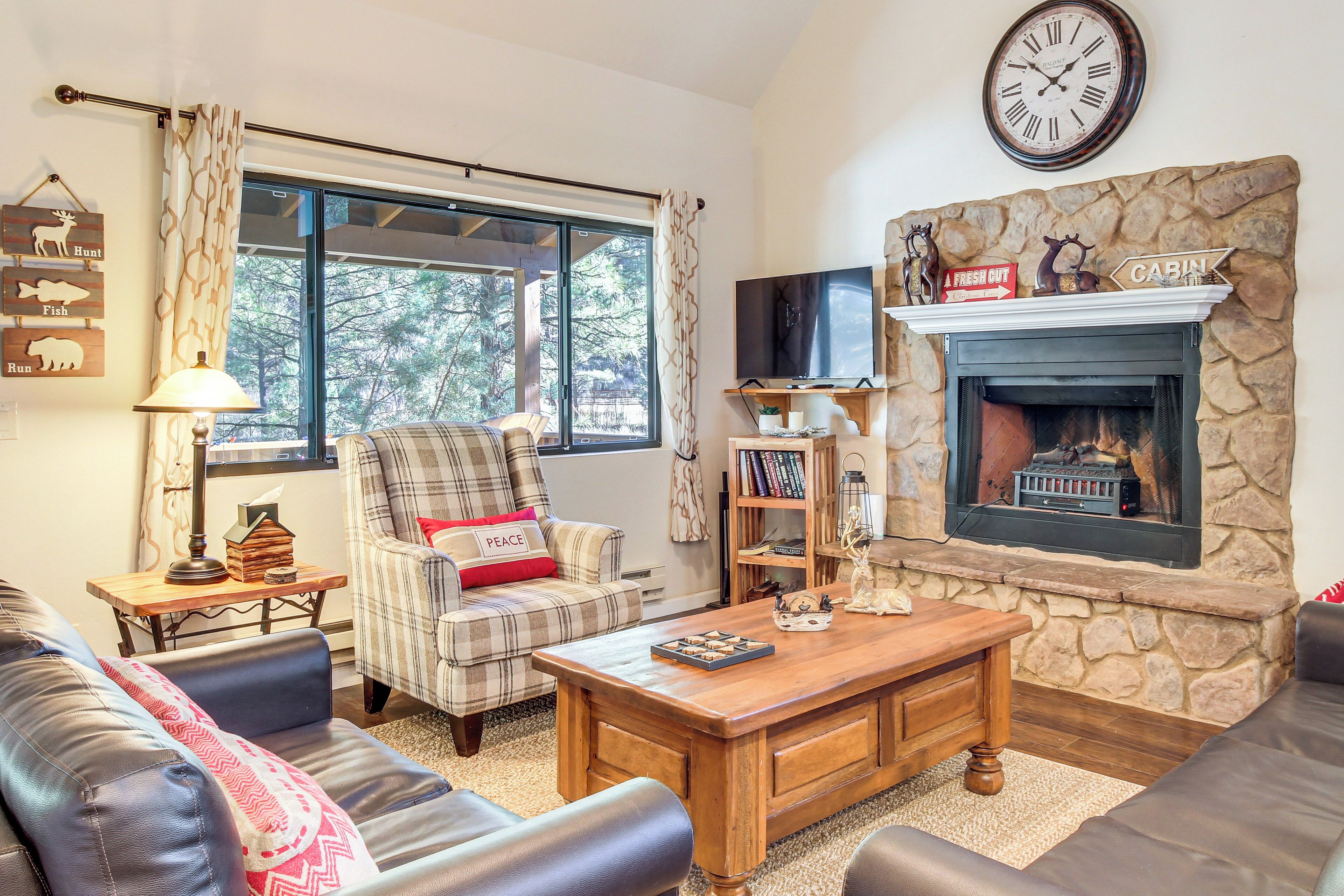 A cozy living room with a fireplace, a plaid armchair, a leather sofa, and a coffee table.