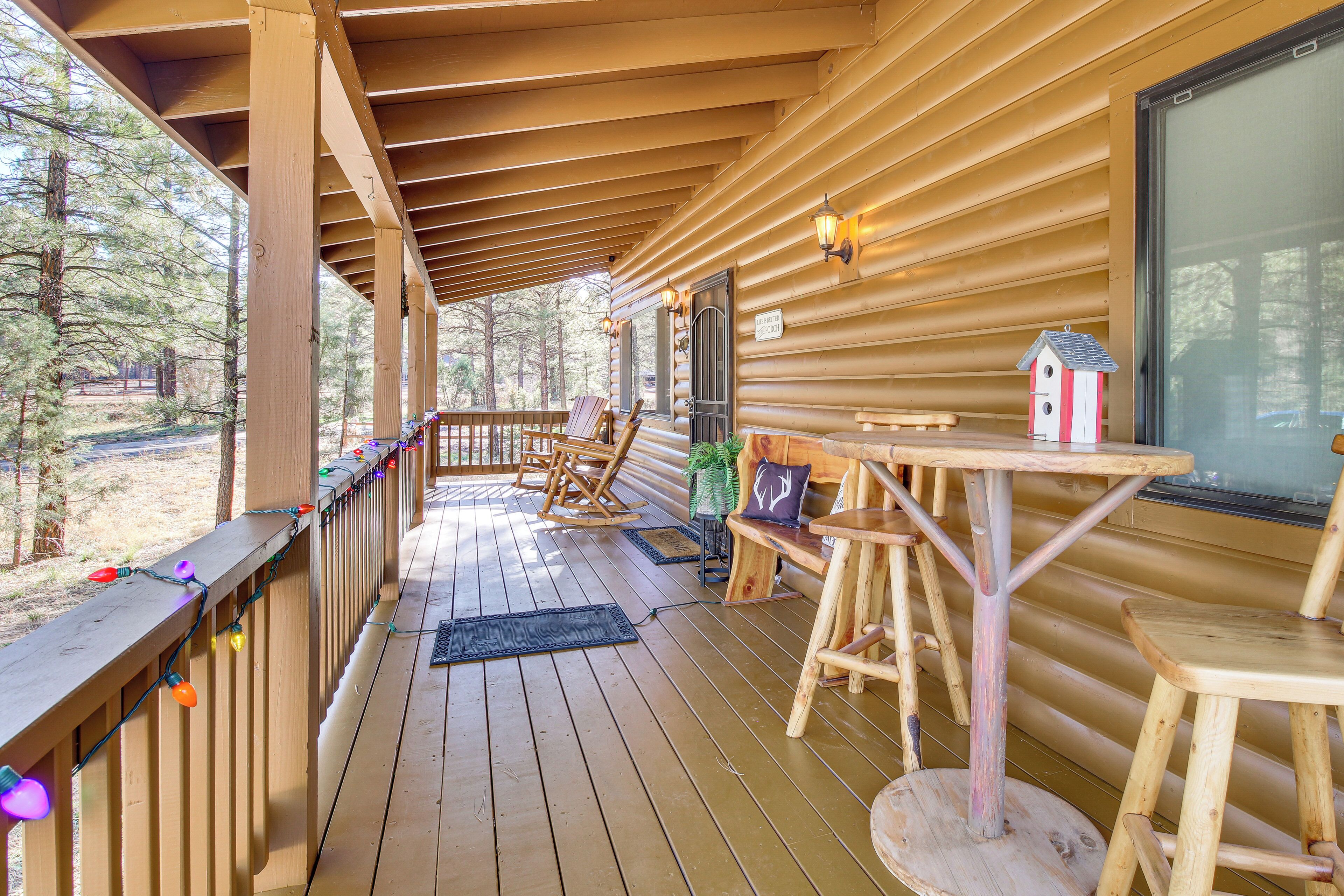 Une terrasse en bois dotée d’un espace abrité, de fauteuils à bascule, d’une petite table et d’une nichoir.