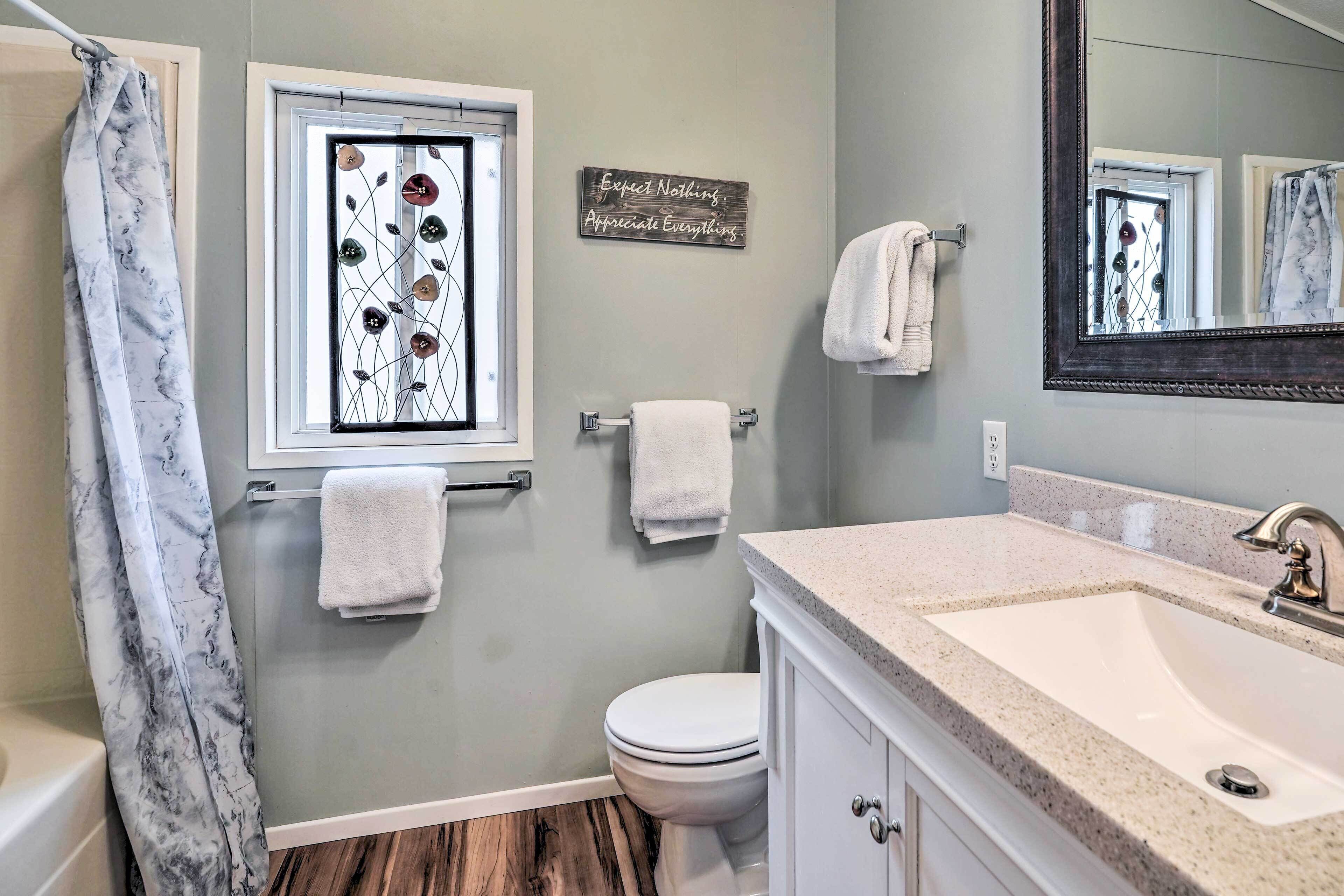 Une salle de bain avec un rideau de douche, une fenêtre ornée de vitraux, des toilettes, un lavabo avec un miroir et un porte-serviettes.