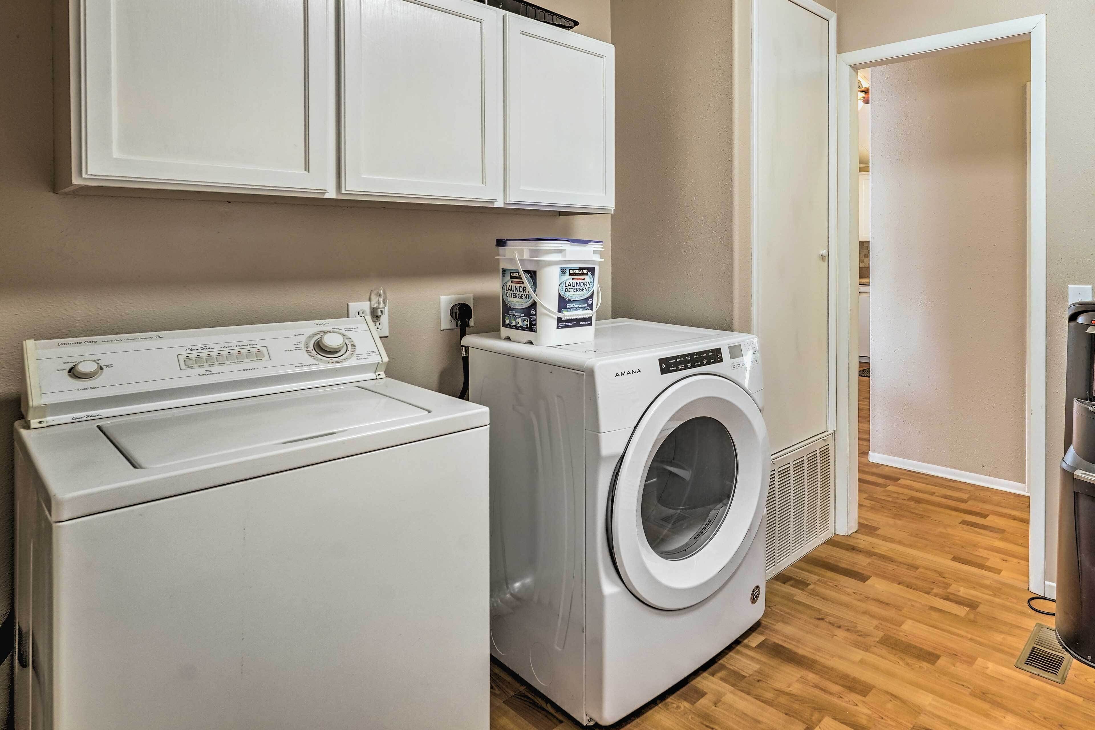 A laundry area with a front-loading washer and dryer, cabinets above, and a wooden floor.