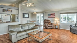 A spacious living room with a leather sofa, a glass coffee table, and a dining area with a chandelier. - Sun-dappled AZ Abode w/ River & Mtn Views! (Parker)
