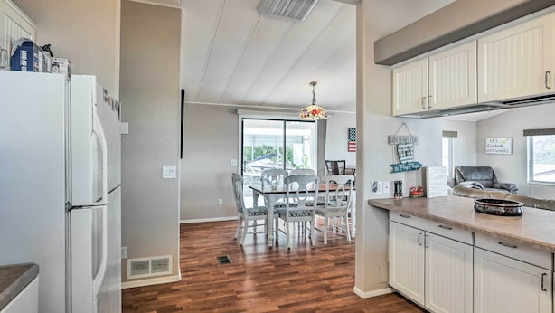A kitchen with white cabinets, a dining area with a table and chairs, and a view to the outside. - Sun-dappled AZ Abode w/ River & Mtn Views! (Parker)
