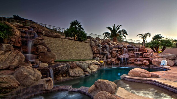 A pool area with a waterfall, rocks, and palm trees. - Patio, Playground! Glendale Family Gem Near Golf (Glendale)