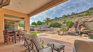 An outdoor patio with stone flooring, a dining area with wooden furniture, and a view of a landscaped garden with a waterfall. - Patio, Playground! Glendale Family Gem Near Golf (Glendale)